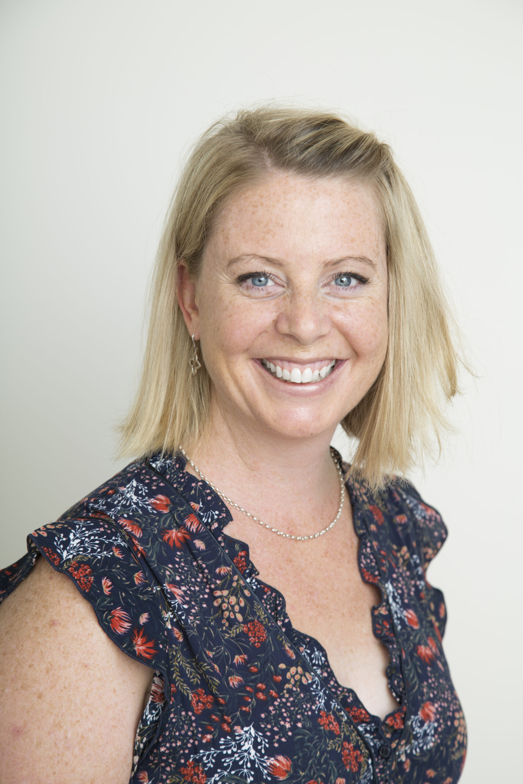 A photo of Kirsty smiling with bright blue eyes, wearing a navy blue floral top.