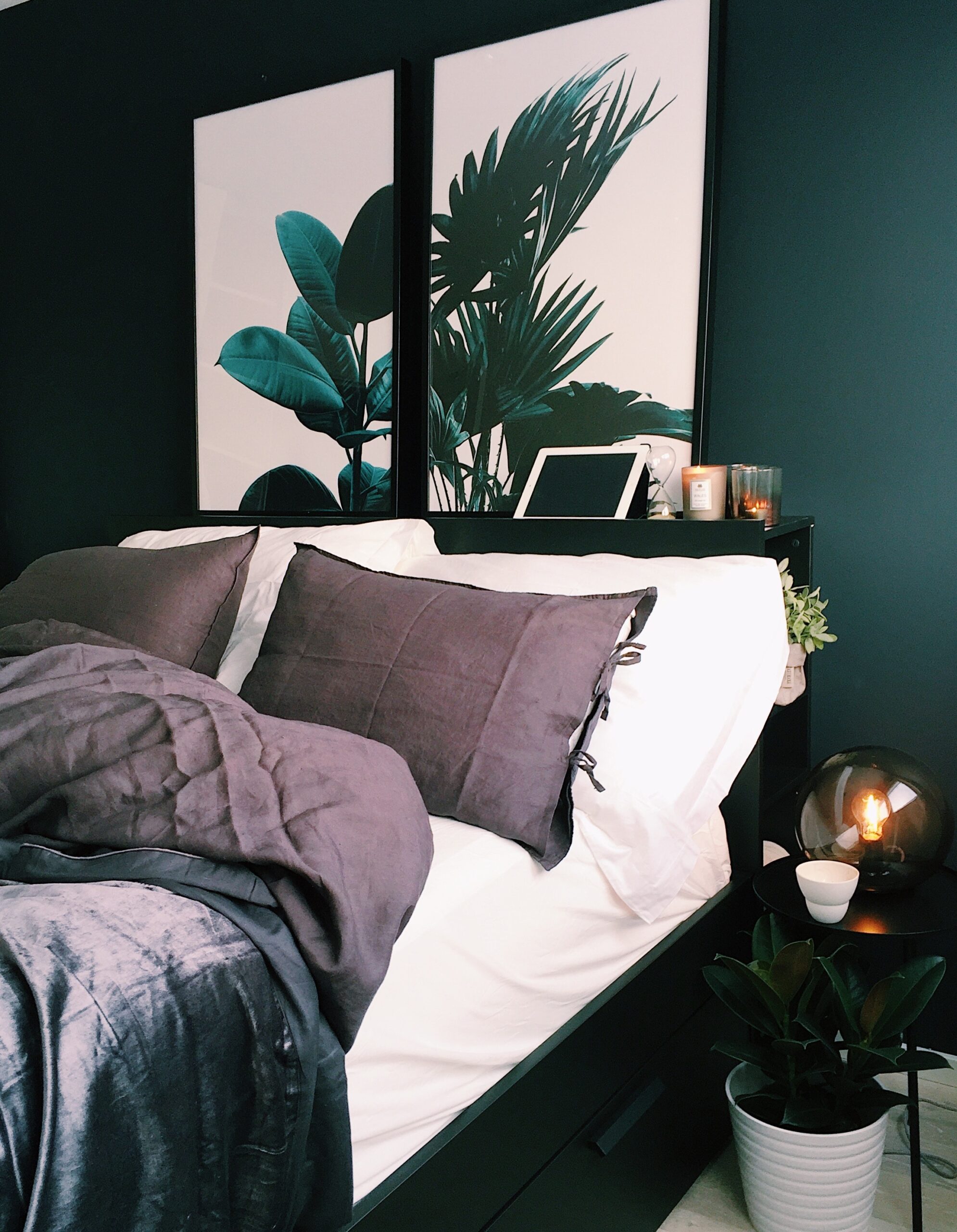 Cosy bed with lots of pillows, a bedhead containing candles and images of lush green leaves.