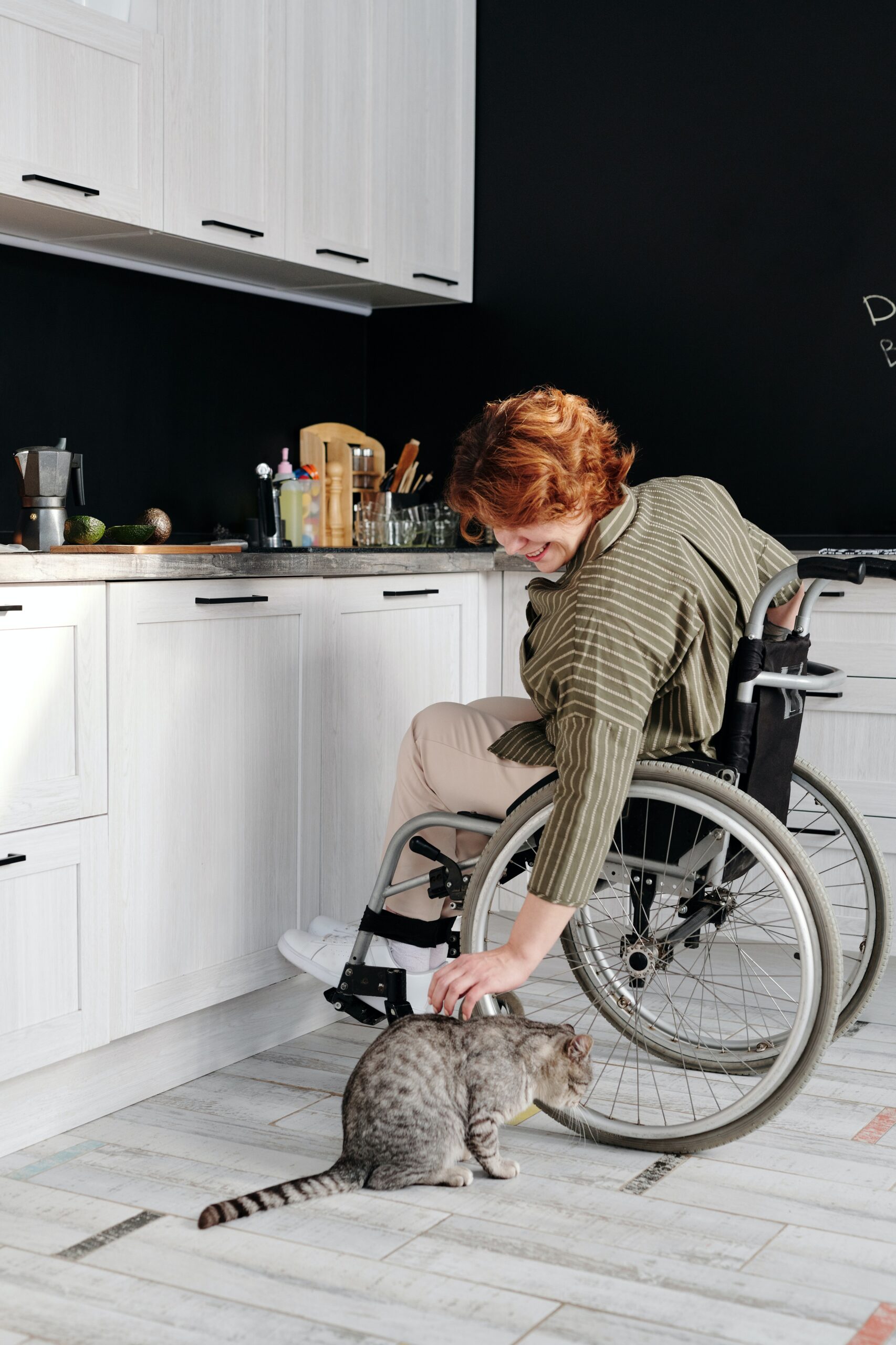 Woman in a kitchen in her wheelchair patting her cat