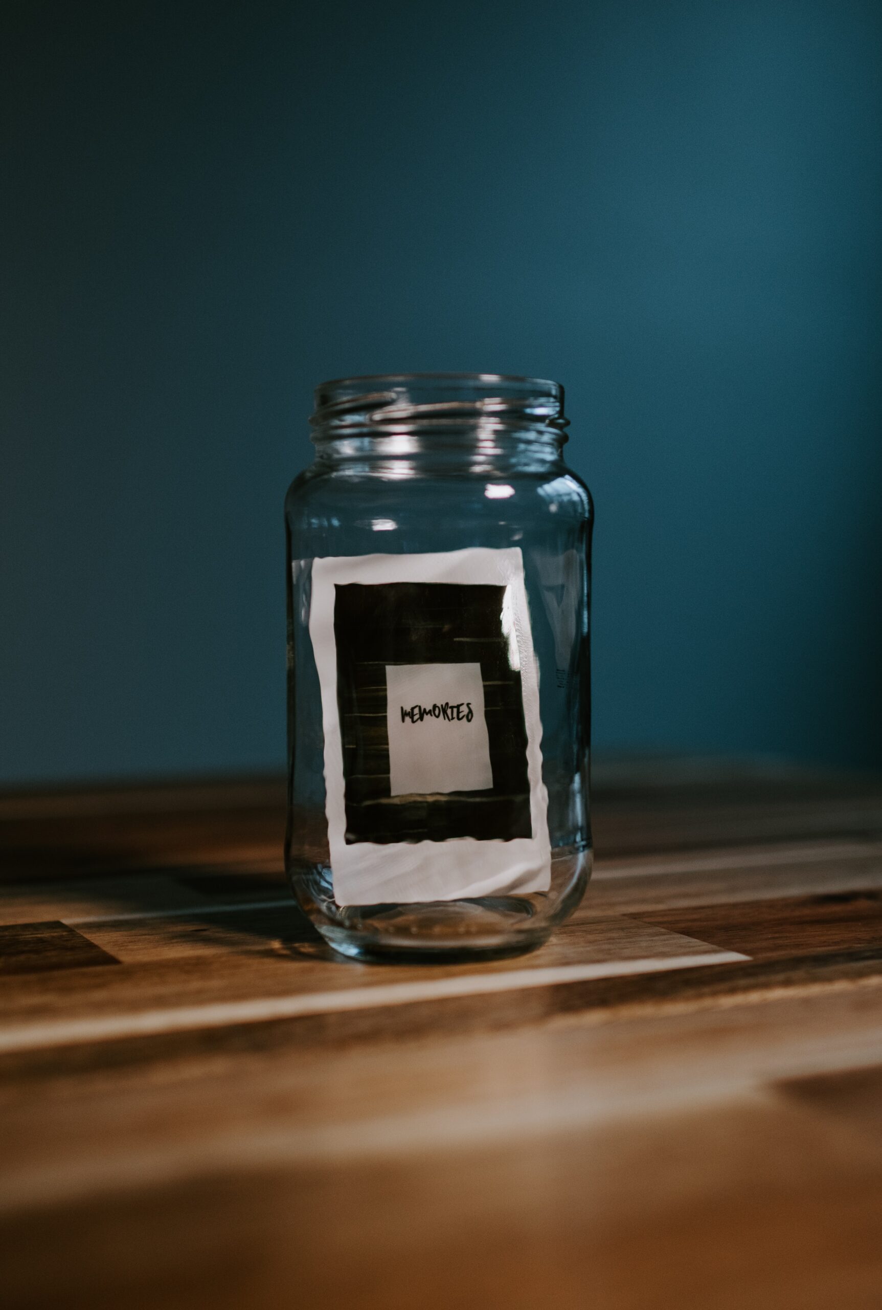 Photo of the word memories in a glass jar on a table top in front of a green wall